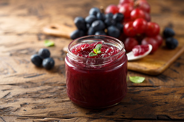 A jar of jam displayed on rustic wooden table, with various berries next to it.